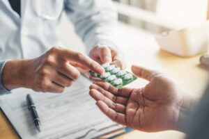 A hand holds several colorful pills above a wooden kitchen table, showing their variety and differences.